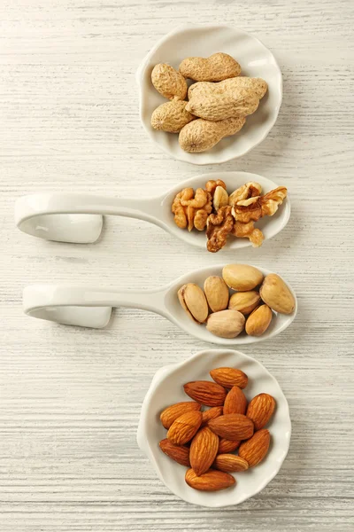 Noci, mandorle, pistacchi, arachidi nei cucchiai di ceramica e ciotole sul tavolo di legno — Foto Stock