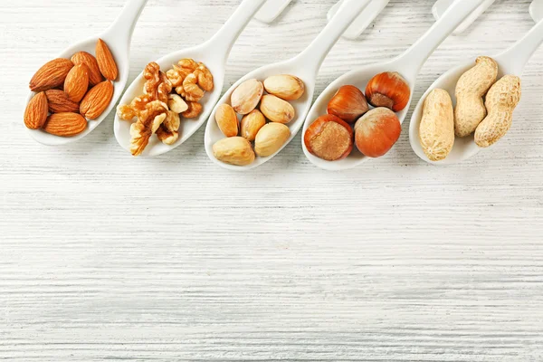 Noci, mandorle, pistacchi, nocciole e arachidi nei cucchiai di ceramica sul tavolo di legno — Foto Stock