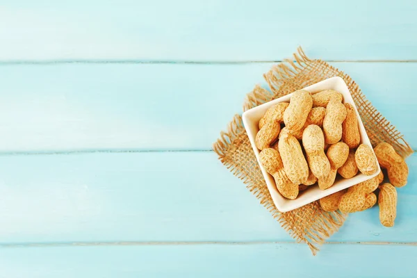 Amendoins na tigela em fundo de madeira azul — Fotografia de Stock