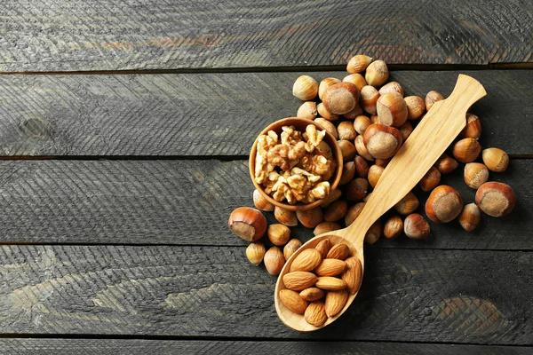 A wooden spoon, a bowl, hazelnuts, walnuts, almonds and acorns on the wooden table — Stock Photo, Image