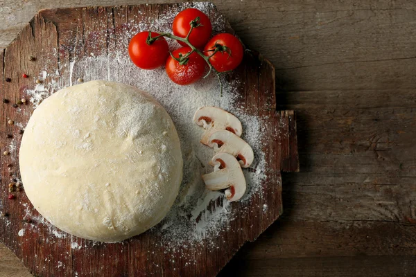 Frisch zubereiteter Teig mit Tomaten und in Scheiben geschnittenen Pilzen auf einem Holzbrett, Nahaufnahme — Stockfoto