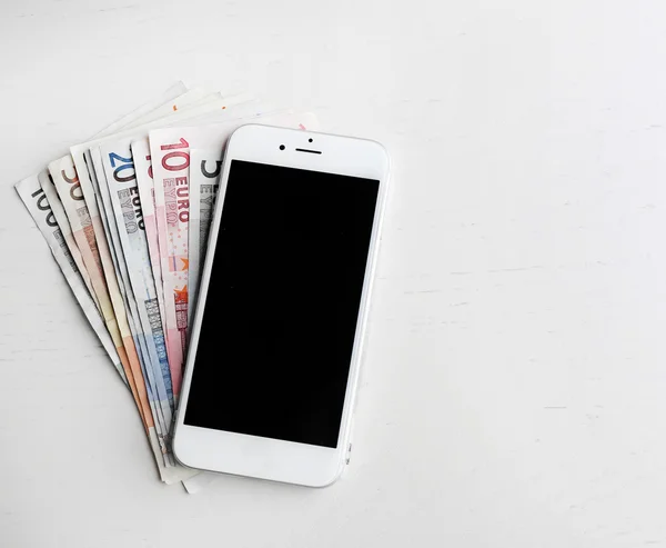 Teléfono inteligente con billetes en euros sobre mesa ligera. Concepto de ganancia de Internet —  Fotos de Stock