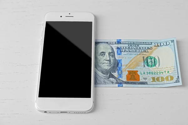Смартфон і банкнота долара на світлому столі. Телефонні збори — стокове фото