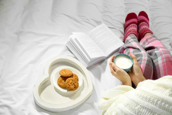 Žena v pyžamu, s knížkou a konzumní mléko na posteli — Stock fotografie