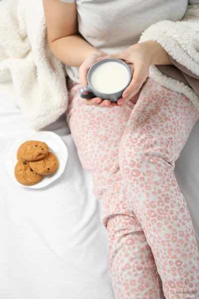 Mujer en pijama sosteniendo una taza de leche en su cama —  Fotos de Stock