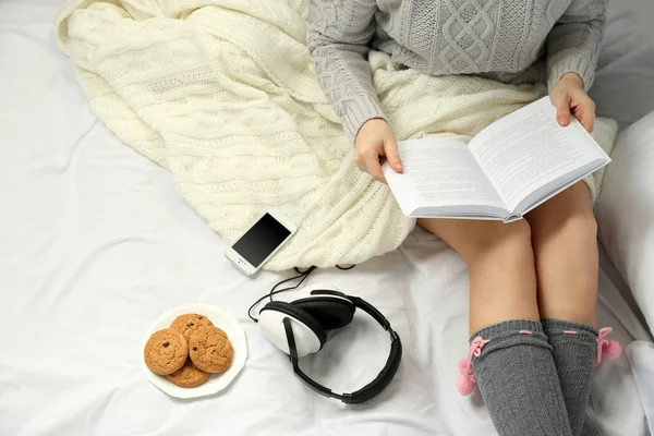 Frau mit Kopfhörern liest ein Buch auf ihrem Bett — Stockfoto