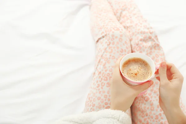 Γυναίκα στο πιτζάμες κρατώντας φλιτζάνι καφέ στο κρεβάτι της — Φωτογραφία Αρχείου