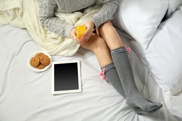 Frau mit Tablette trinkt Orangensaft auf ihrem Bett — Stockfoto