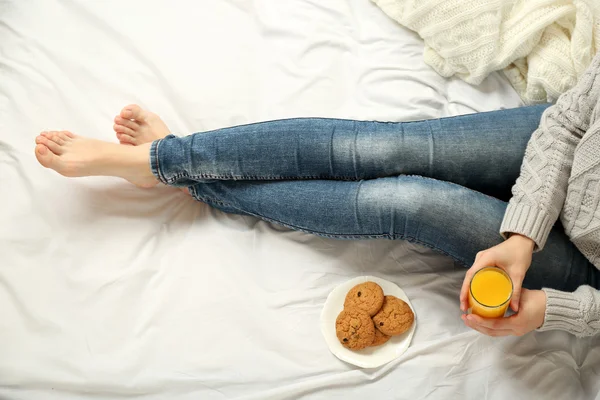 Mujer bebiendo jugo de naranja con galletas en su cama — Foto de Stock