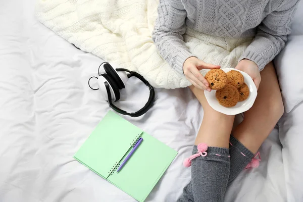 Mulher com fones de ouvido e diário comer biscoitos em sua cama — Fotografia de Stock