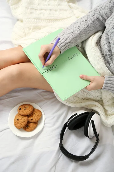 Frau mit Kopfhörer schreibt Tagebuch auf ihrem Bett — Stockfoto