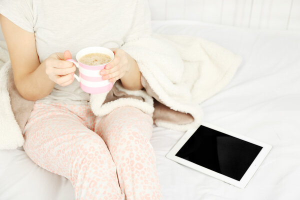 Woman in pajamas with tablet drinking coffee 