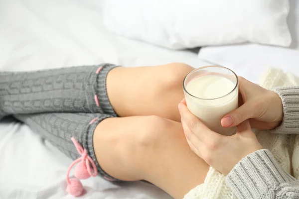 Kobieta siedzi i trzymając szklankę mleka na jej łóżko — Zdjęcie stockowe