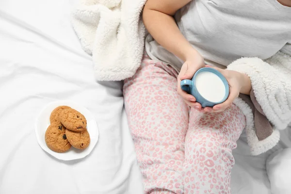 Mujer en pijama sosteniendo una taza de leche en su cama —  Fotos de Stock