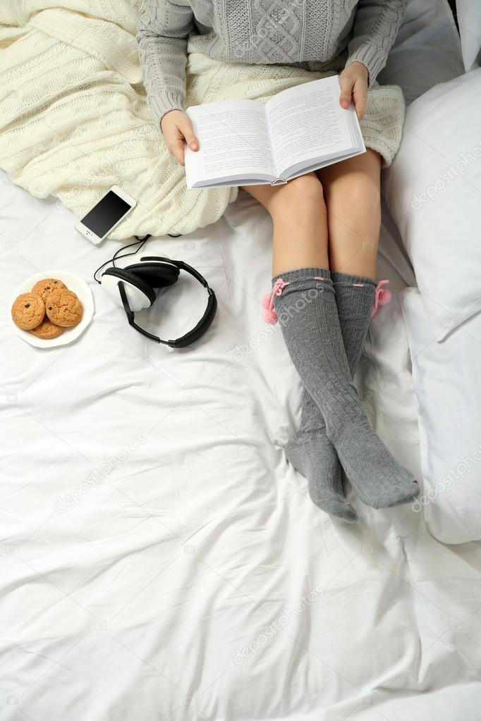 Woman with headphones reading a book on her bed
