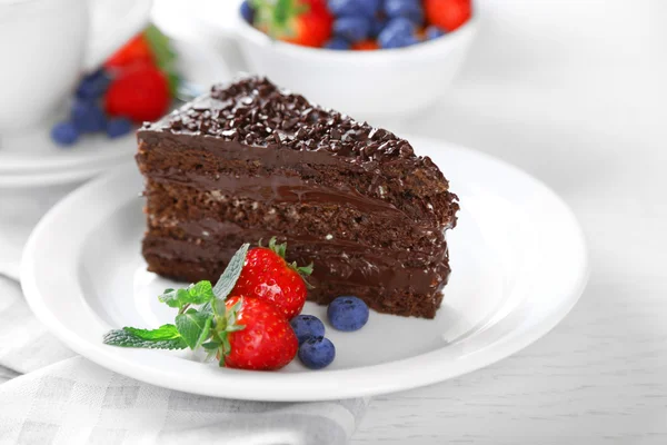 Schokoladenkuchen mit Schokoladencreme und frischen Beeren auf Teller, auf hellem Hintergrund — Stockfoto