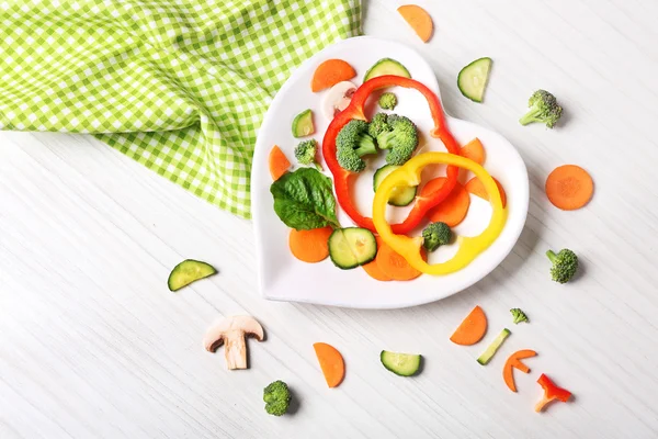 Useful cut vegetables on a plate in the form of heart on wooden table top view — Stock Photo, Image