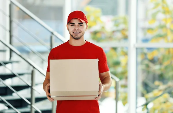 Postbote in roter Uniform hält Paket — Stockfoto