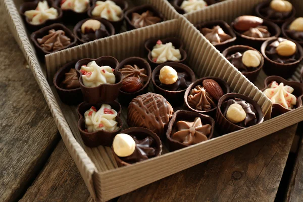 Verschillende chocolade snoepjes in papier vak op houten achtergrond, close-up — Stockfoto