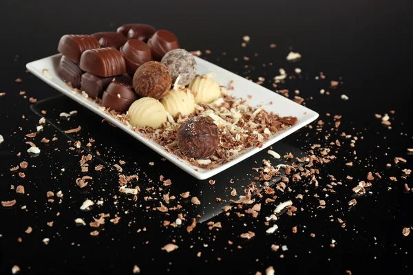 Assorted chocolade snoepjes op wit bord met vlokken op zwarte achtergrond — Stockfoto