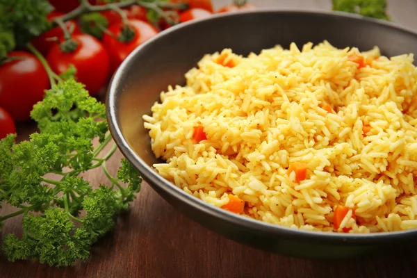 Stewed rice with a carrot on a black plate over wooden background, close up — Stock Photo, Image