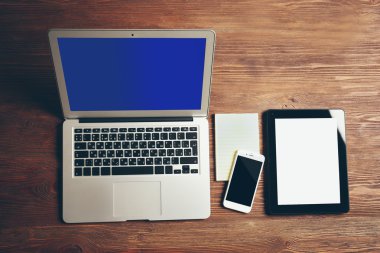 Modern dizüstü bilgisayar, cep telefonu, tablet ve ahşap masa üstünde defter