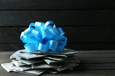 Ahşap arka plan üzerinde hediye olarak yay ile dolar yığını