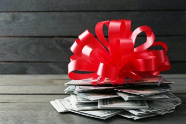 Ahşap arka plan üzerinde hediye olarak yay ile dolar yığını