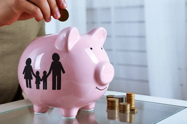 Man puts coin into a piggy-bank — Stock Photo, Image