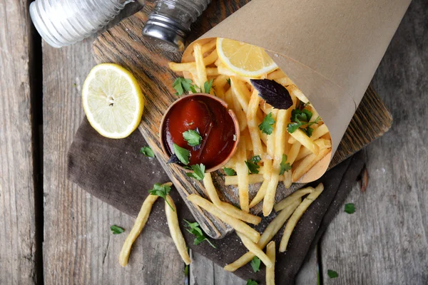 Batatas fritas francesas em papel artesanal na tábua de corte — Fotografia de Stock