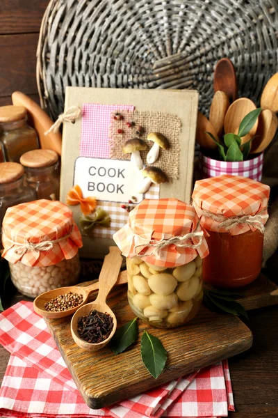 Potten met ingemaakte groenten en bonen, specerijen, boek recepten en keukengerei op houten achtergrond — Stockfoto