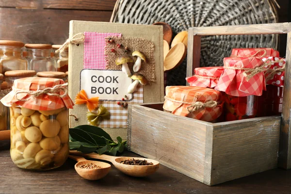 Jars with pickled vegetables, beans, spices and kitchenware on wooden background — Stock Photo, Image