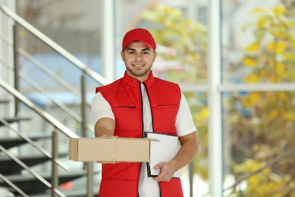 Pošťák v červené uniformě drží balíček — Stock fotografie