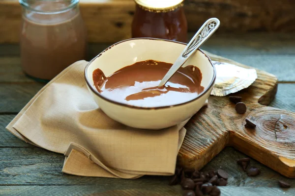 Melted chocolate in glass bowl, on wooden background — Stock Photo, Image