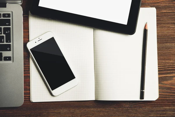 Moderní notebook, mobilní telefon, tablet a poznámkového bloku na dřevěný stůl, detail — Stock fotografie