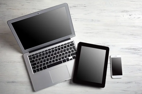 Laptop moderno, telefone celular e tablet em fundo de madeira branca — Fotografia de Stock