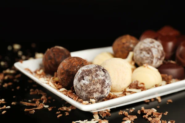 Doces de chocolate sortidas na placa branca com flocos sobre fundo preto — Fotografia de Stock