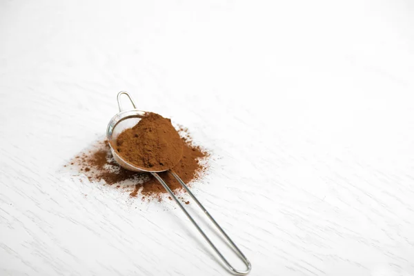 Colador con polvo de cacao sobre mesa blanca —  Fotos de Stock