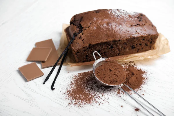Шоколадный торт с какао-порошком, ванильные стручки на белом столе — стоковое фото