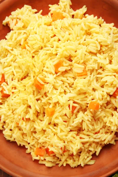 Stewed rice with a carrot on a brown plate, close up — Stock Photo, Image