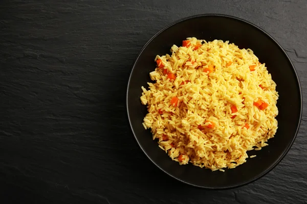 Stewed rice with a carrot on a plate over black background — Stock Photo, Image