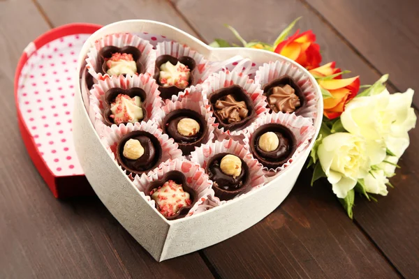 Heart shaped box with candies and flowers on a wooden background, close up — Stock Photo, Image