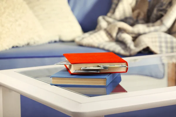 Красные и синие книги со спрятанными долларовыми банкнотами на стеклянном столе — стоковое фото
