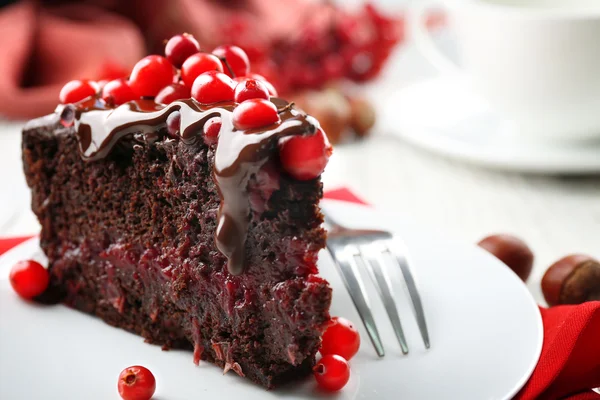 Piece of chocolate cake with cranberries on plate with nuts on wooden table, closeup — Stock Photo, Image