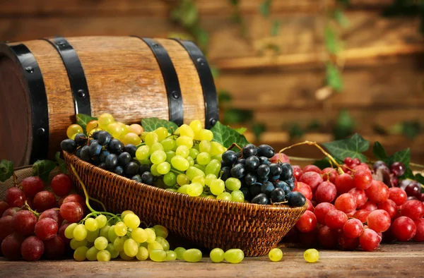 Виноград в чаше и бочке на деревянном столе — стоковое фото