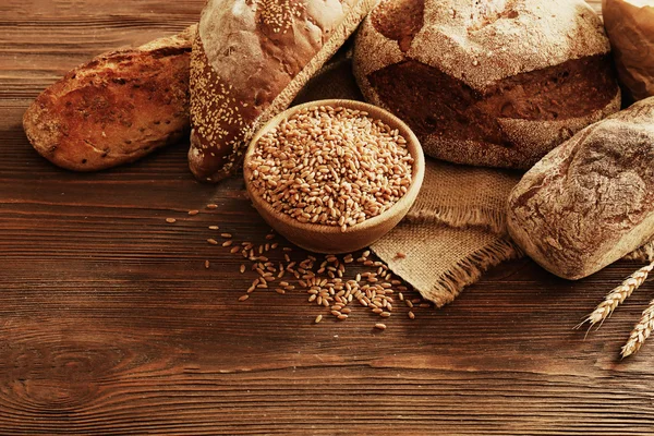 Pane appena sfornato e una ciotola di chicchi di grano sullo sfondo di legno — Foto Stock