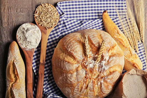 Pane appena sfornato, farina, grano in cucchiai e tovagliolo in tavola, primo piano — Foto Stock