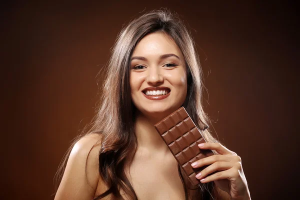 Portrait of attractive young woman with chocolate on brown background, close up — Stock Photo, Image