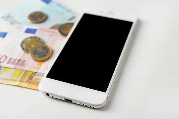 Teléfono inteligente y billetes en euros con monedas en la mesa de luz. Tarifas telefónicas —  Fotos de Stock