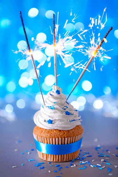 Cupcake with white cream icing and sparklers on a glitter background, close up